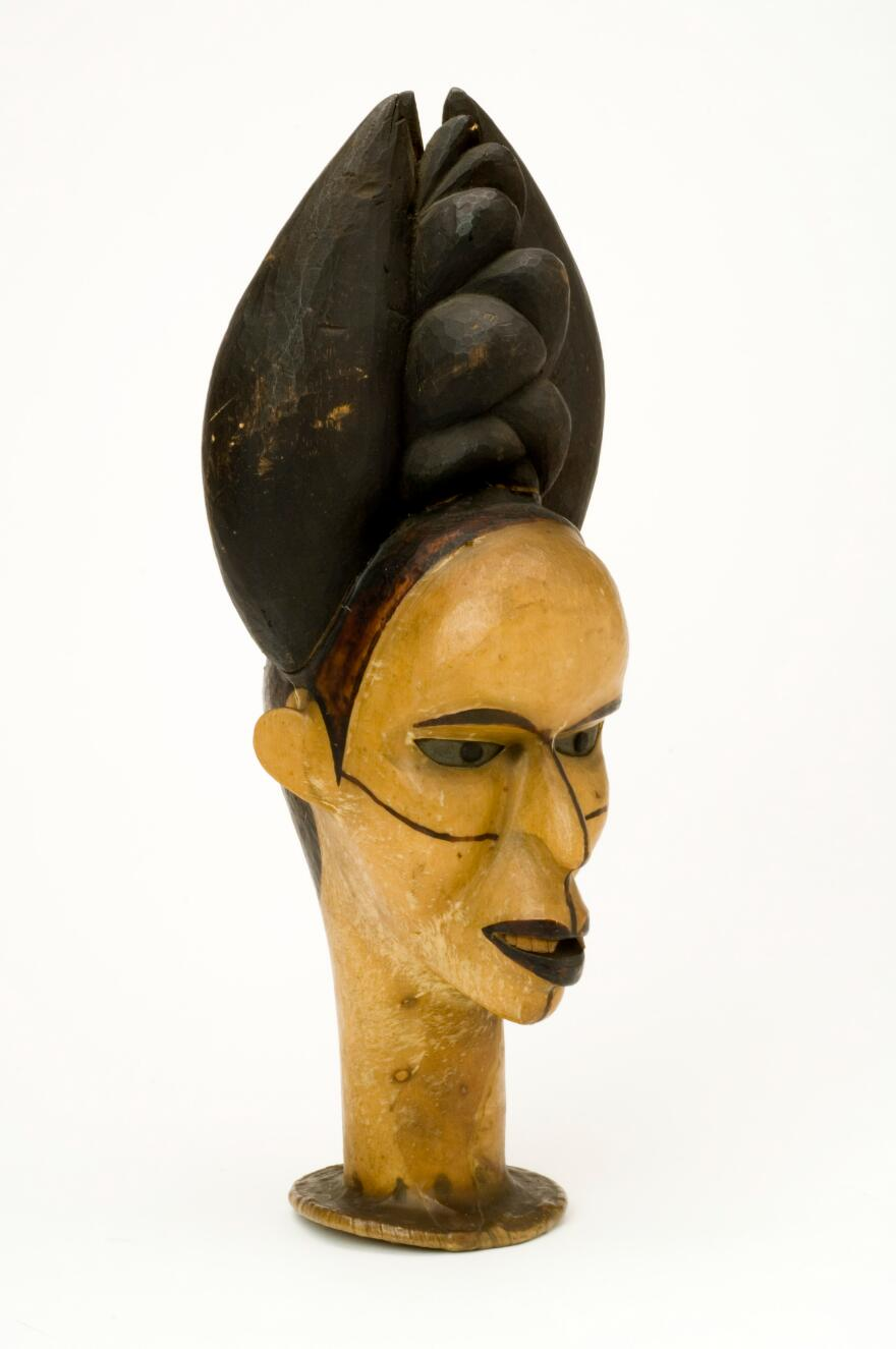 A female head with elaborate coiffure from the Ibo People, West Africa. The wooden headdress is covered with skin and has eyes of zinc.